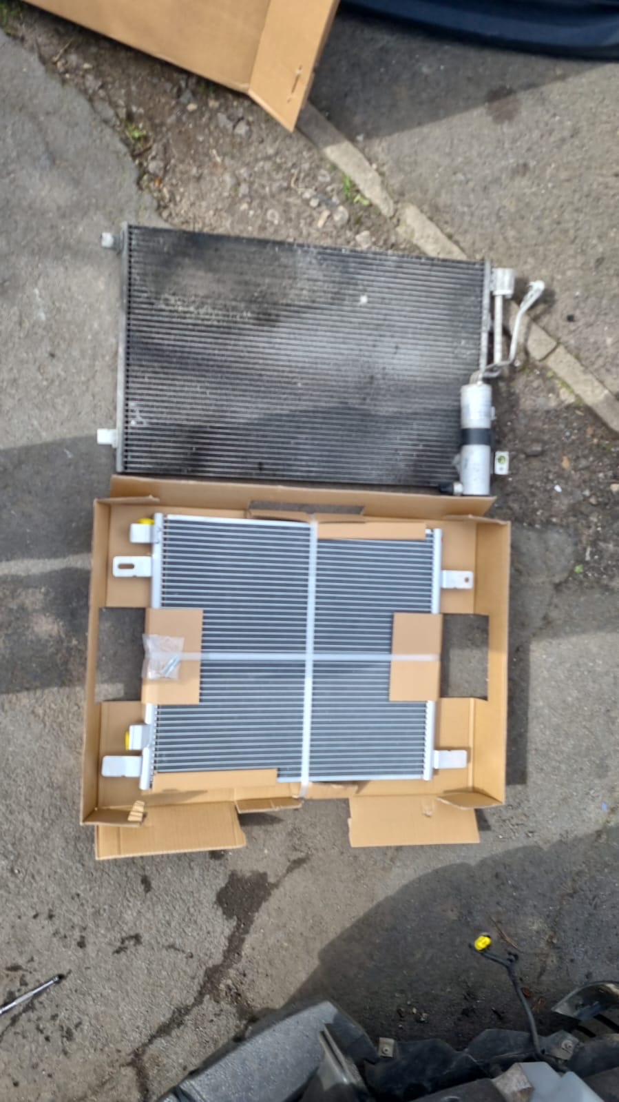 Old corroded air conditioning condenser next to a brand new replacement condenser in its box